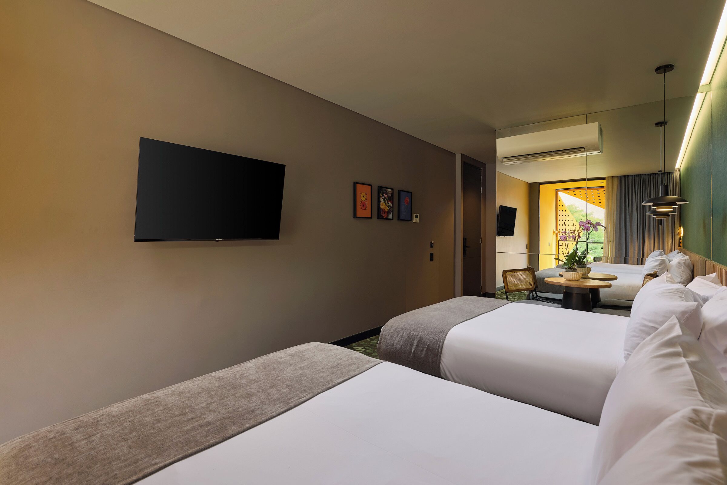 A hotel room with two beds, a flat-screen TV, a small table with a plant, and a view of the outdoors.