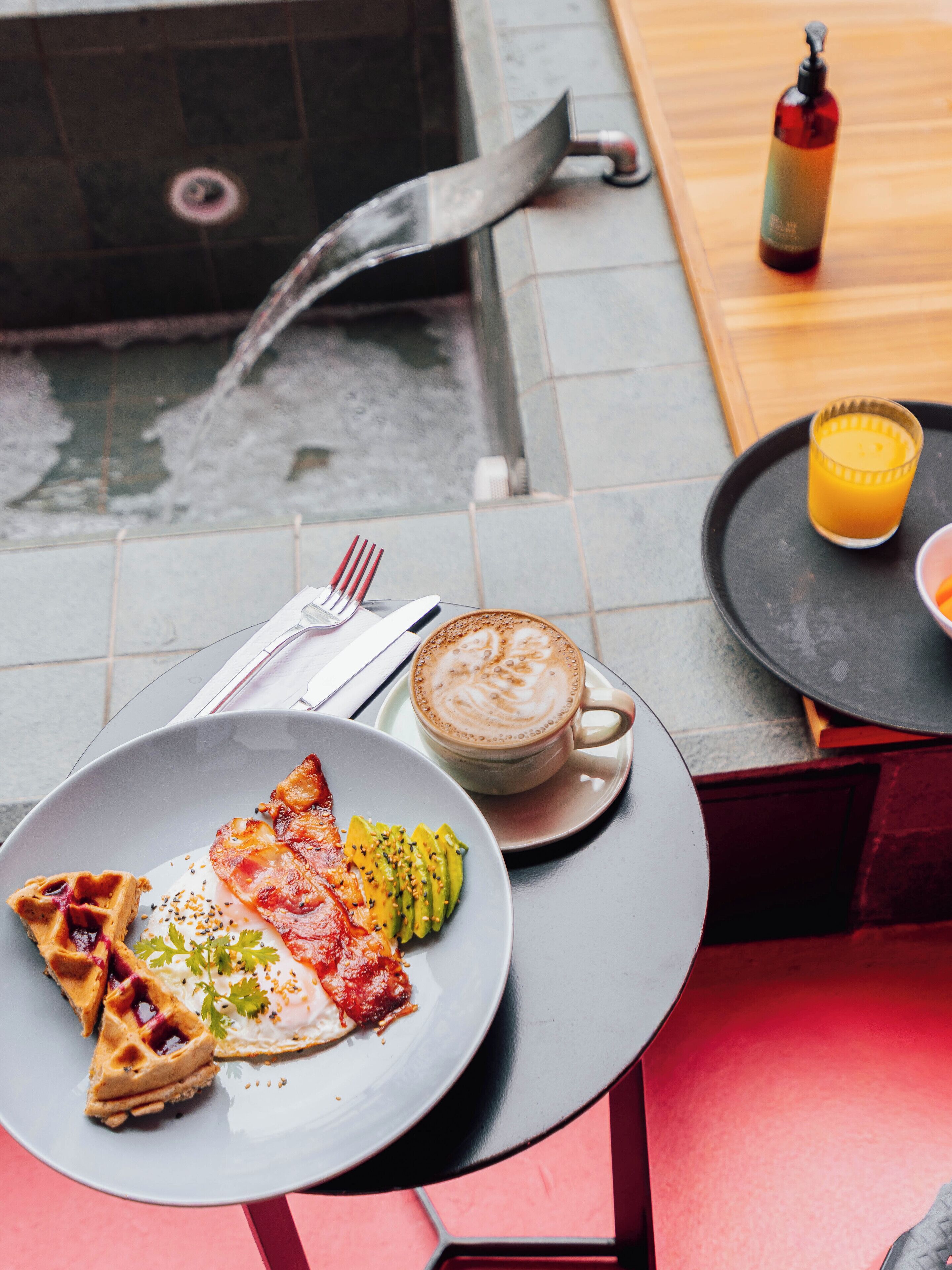 A breakfast setting with waffles, eggs, and avocado on a plate, a cup of coffee, and a glass of orange juice on a table.