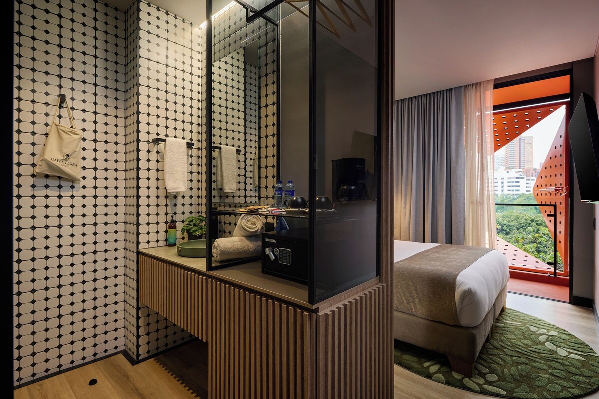 Une chambre d’hôtel avec un grand miroir, un lit, une table de chevet avec une plante, une serviette et une machine à café.