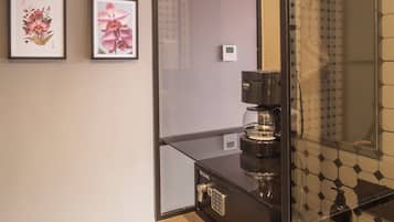 Un baño moderno con cabina de ducha de vidrio, una cafetera y dos cuadros con motivos florales en la pared.