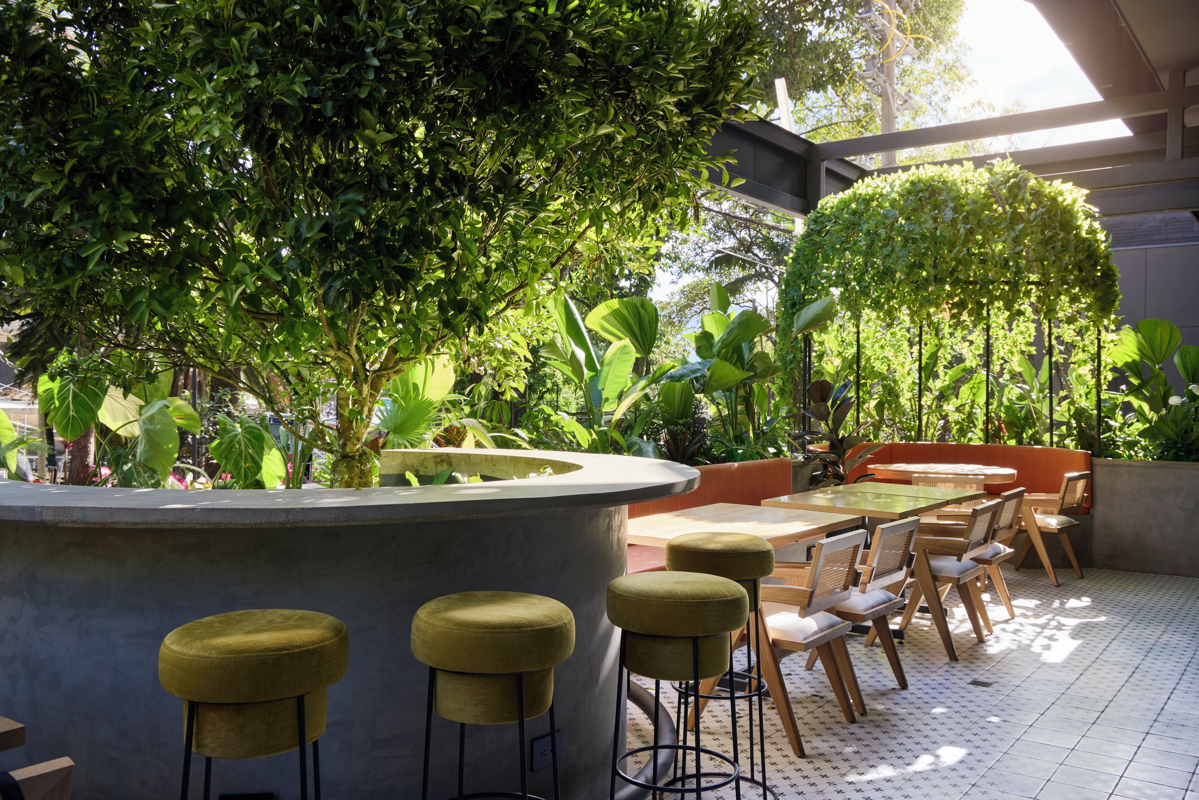 An outdoor seating area with a round table and bar stools, surrounded by lush greenery and potted plants.