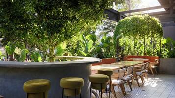 An outdoor seating area with a round table and bar stools, surrounded by lush greenery and potted plants.