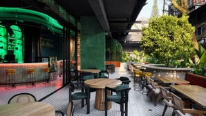 Een terras met ronde tafels en stoelen, een bar en beplanting.