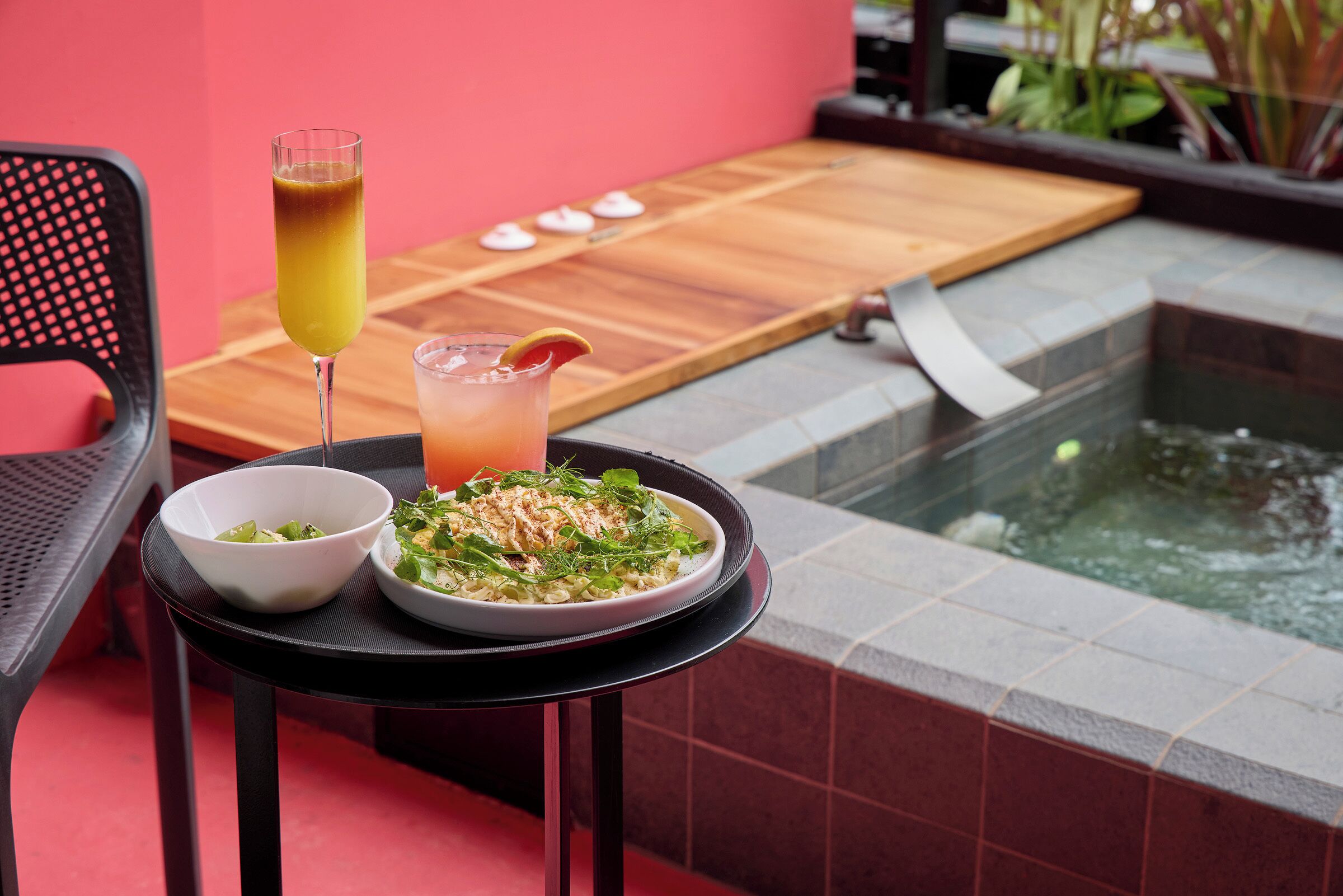 Ett matbord med en skål med sallad och en tallrik med mat, ett glas juice och en träbricka med små föremål.