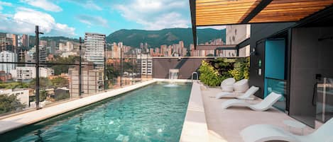 Una piscina en la azotea con agua cristalina, vistas panorámicas de la ciudad y sillones de descanso modernos.