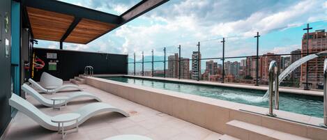 Área de piscina en la azotea con sillones y vistas al horizonte de la ciudad.
