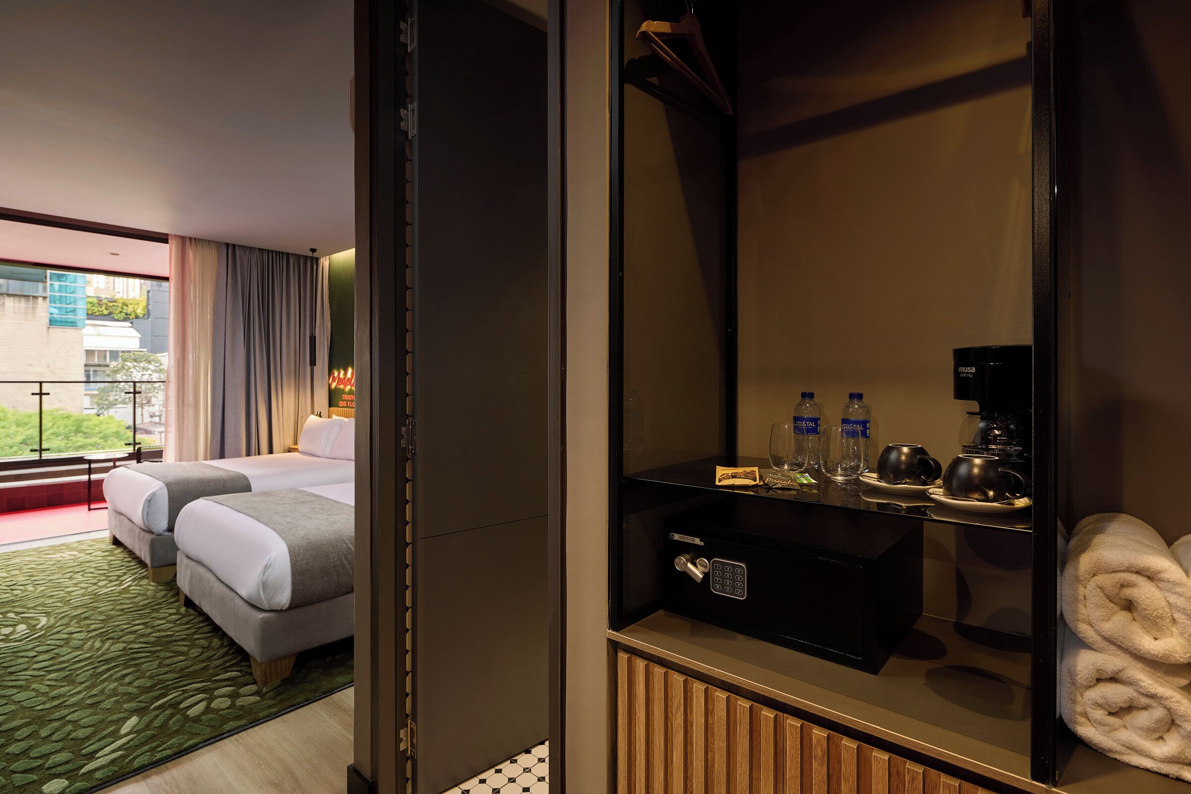 Ett hotellrum med två sängar, en minibar, en spegel och utsikt över omgivningarna.