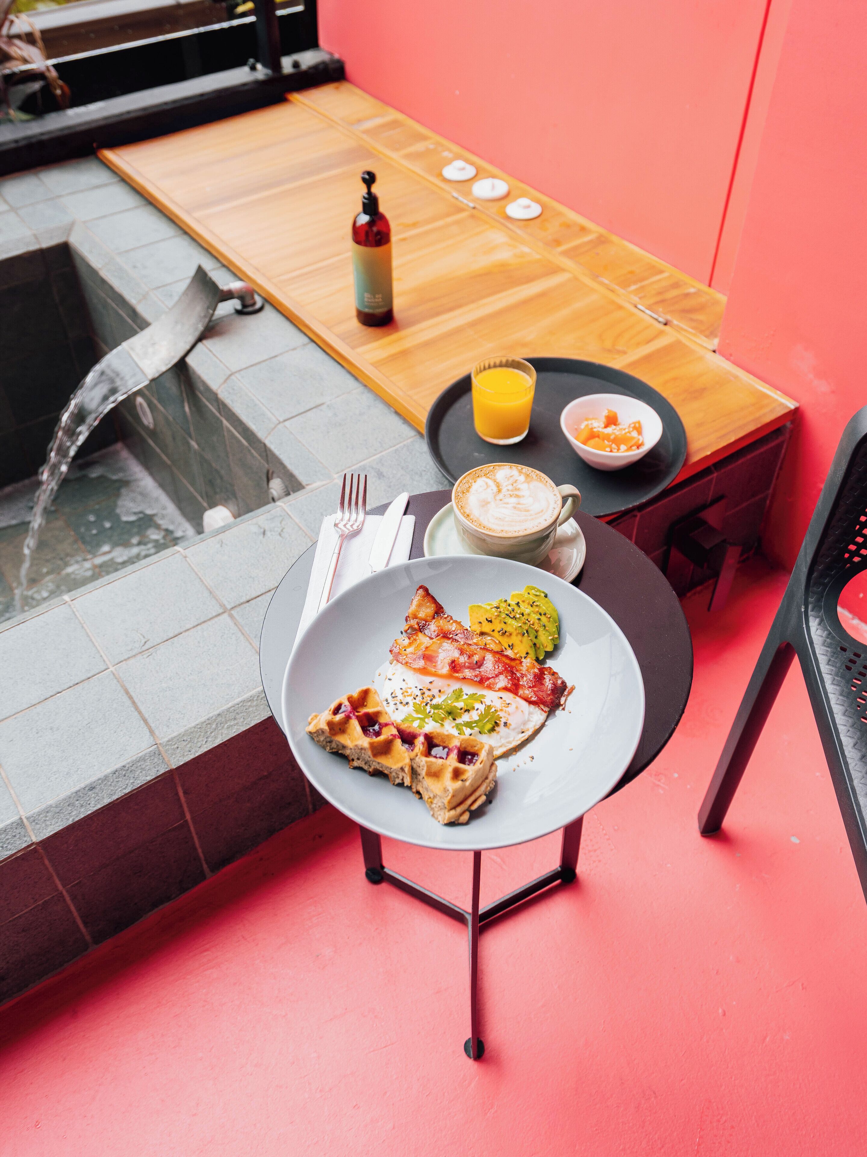 A breakfast setting with a waffle, eggs, bacon, and fruit on a plate, a cup of coffee, and a glass of orange juice on a table.