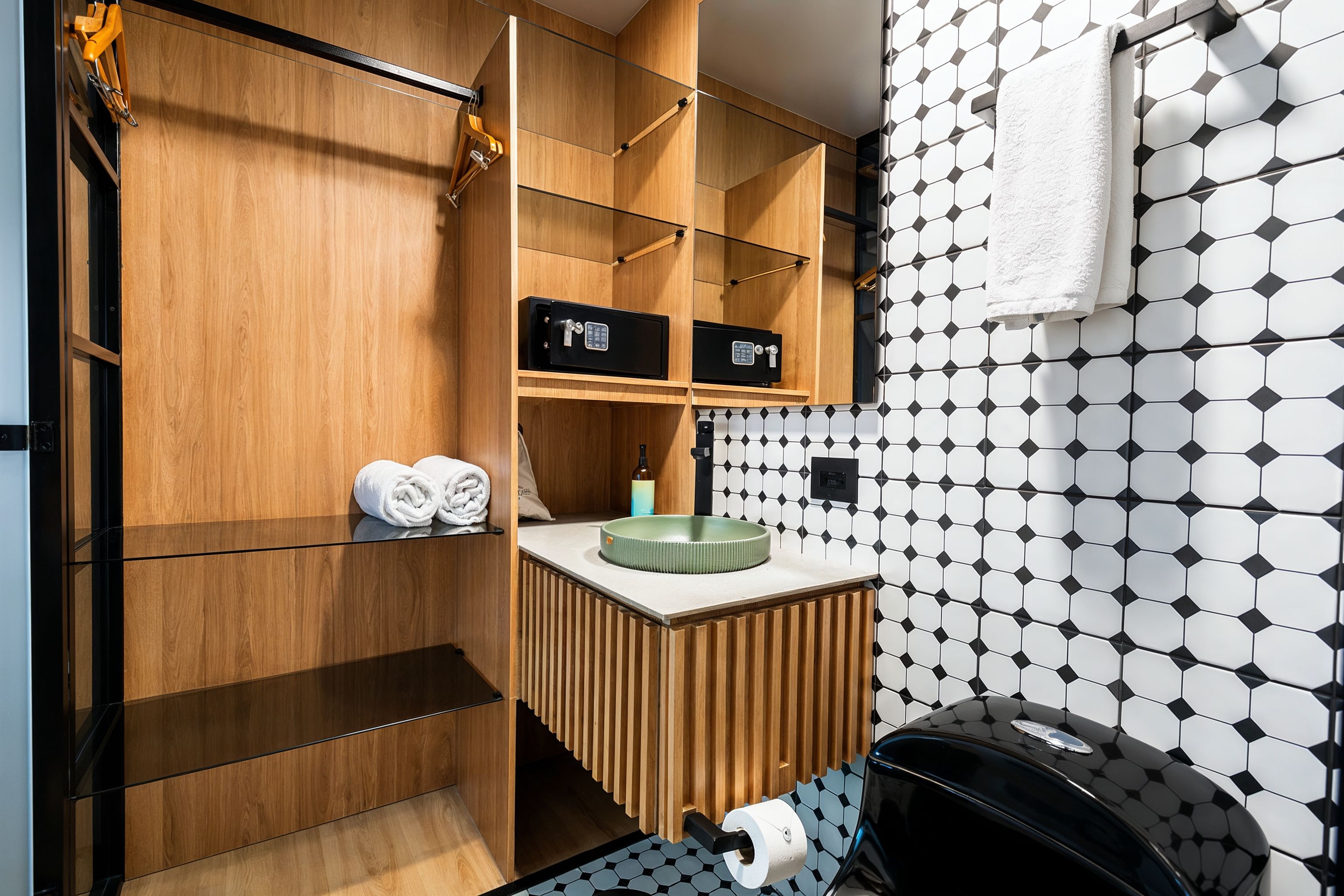 Un baño moderno con tocador de madera, dos cajas fuertes negras, un perchero y un dispensador de papel higiénico.