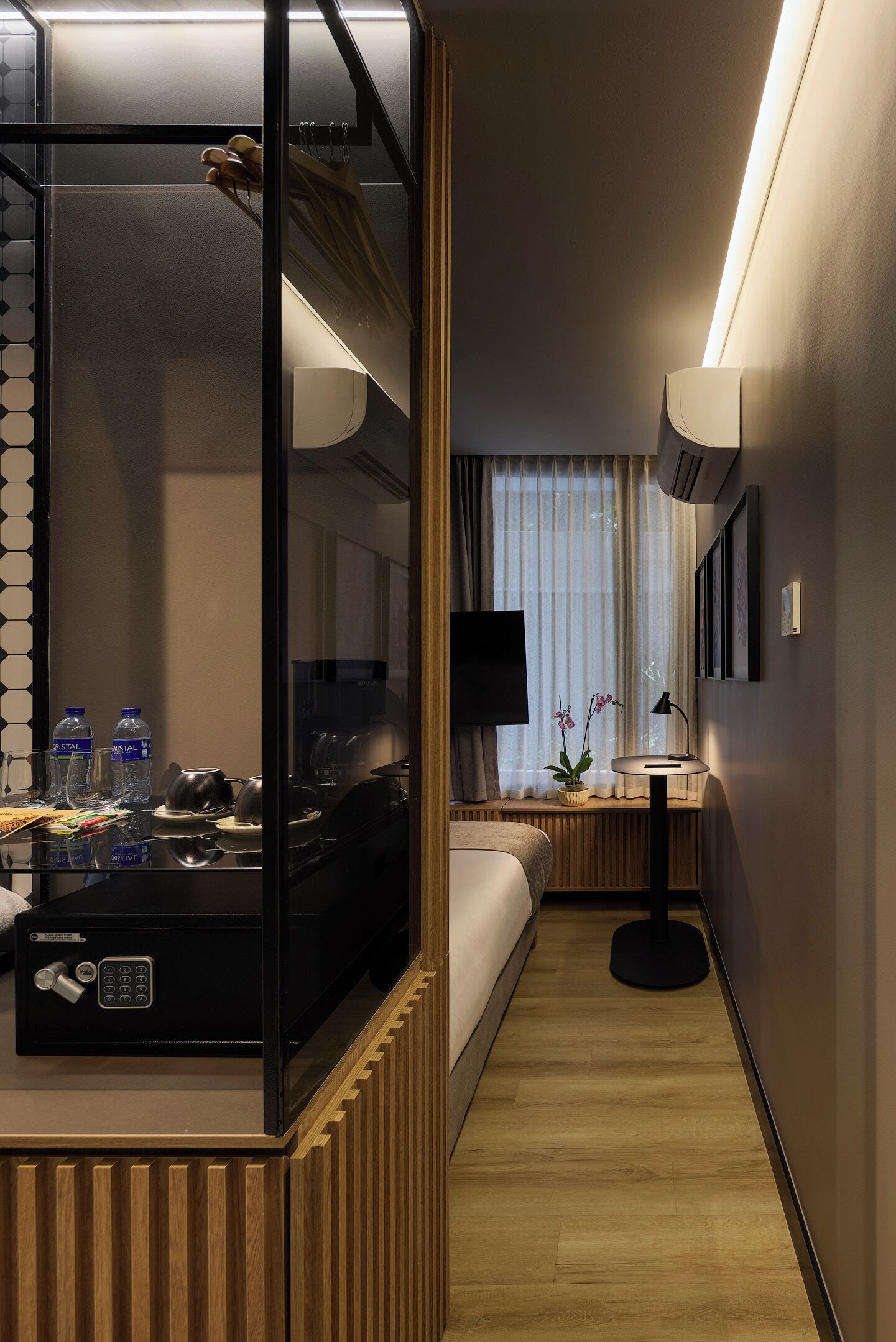 A hotel room with a bed, bedside table, lamp, TV, and a window with curtains.
