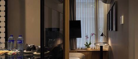 A hotel room with a bed, bedside table, lamp, TV, and a window with curtains.
