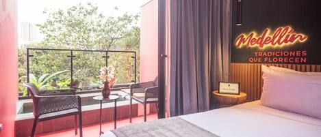 A hotel room with a balcony, a bed, a nightstand, and a sign reading "Medellin Tradiciones Que Florecen."