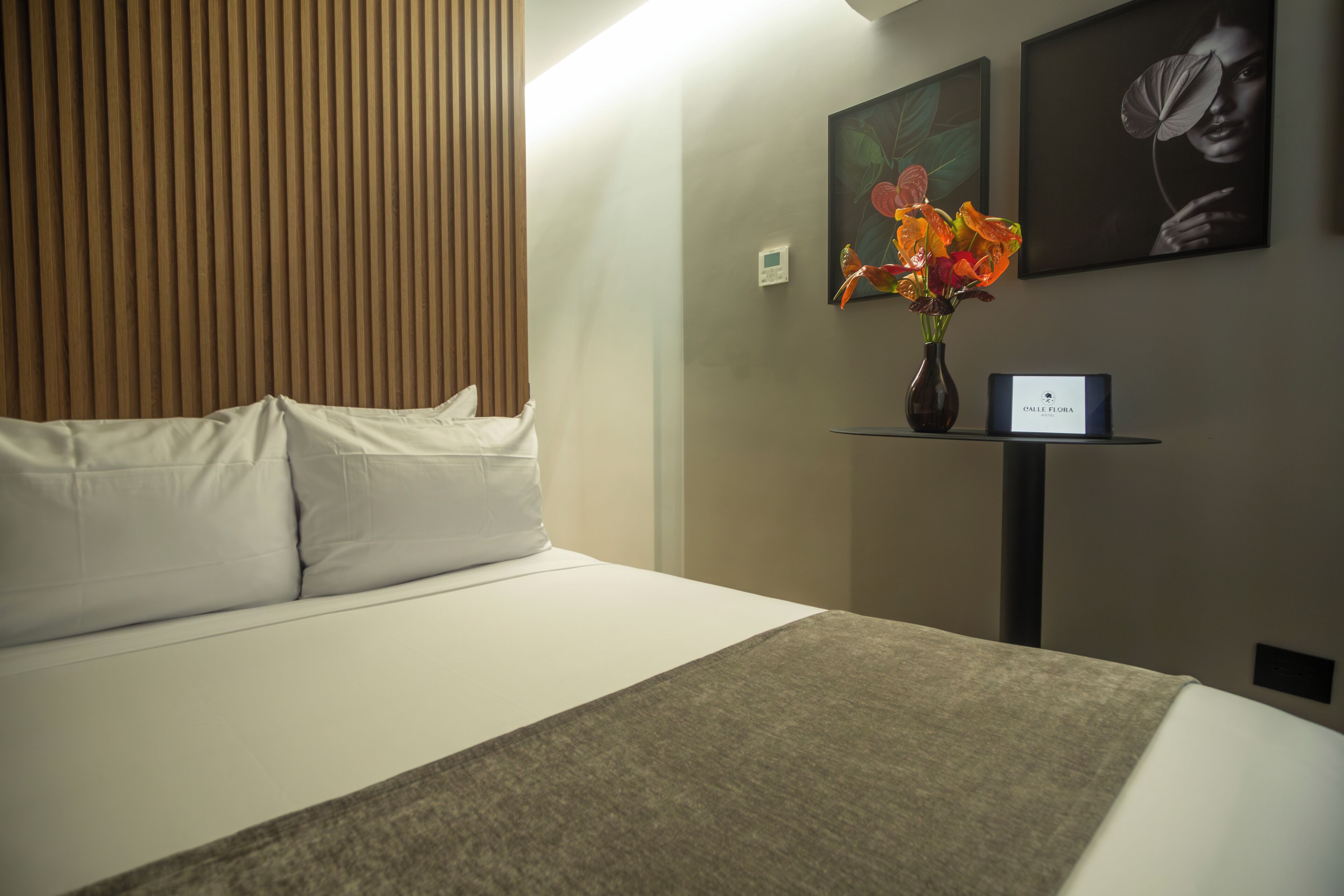 A hotel room with a bed, a nightstand with a vase of flowers, and two framed pictures on the wall.