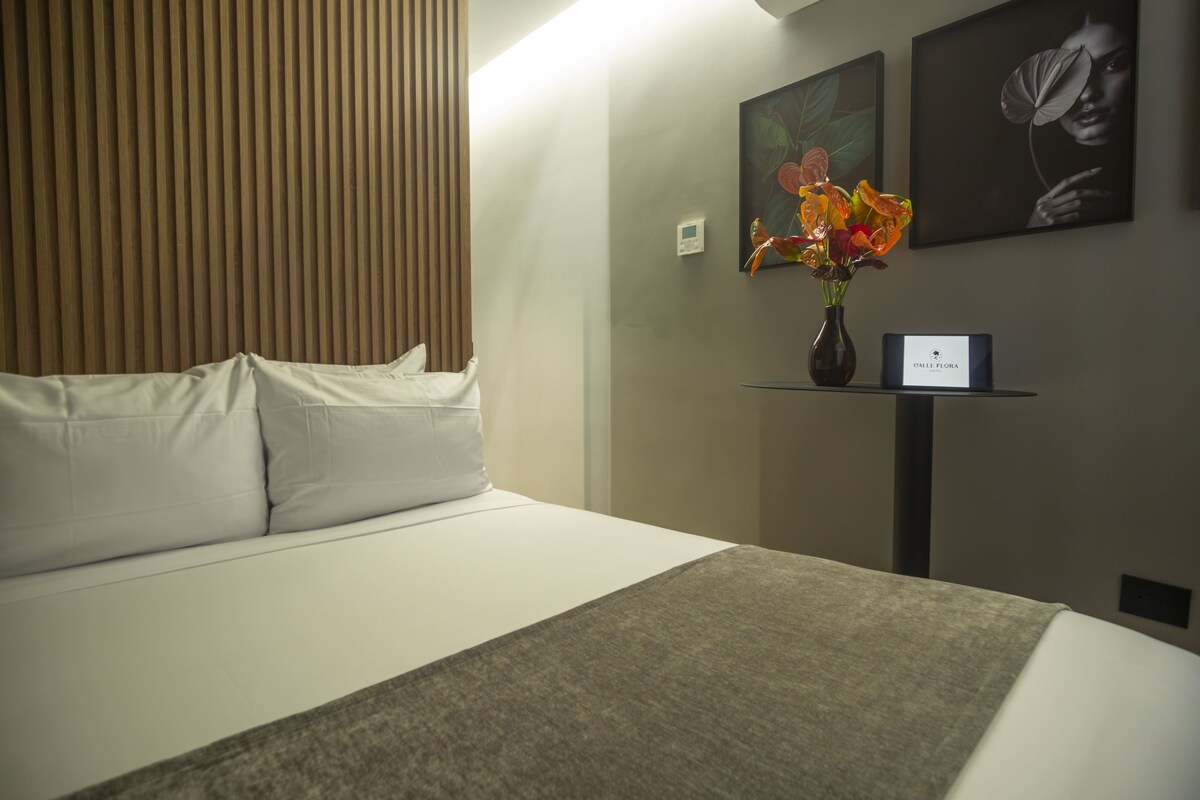 A hotel room with a bed, a vase with flowers, and two framed pictures on the wall.