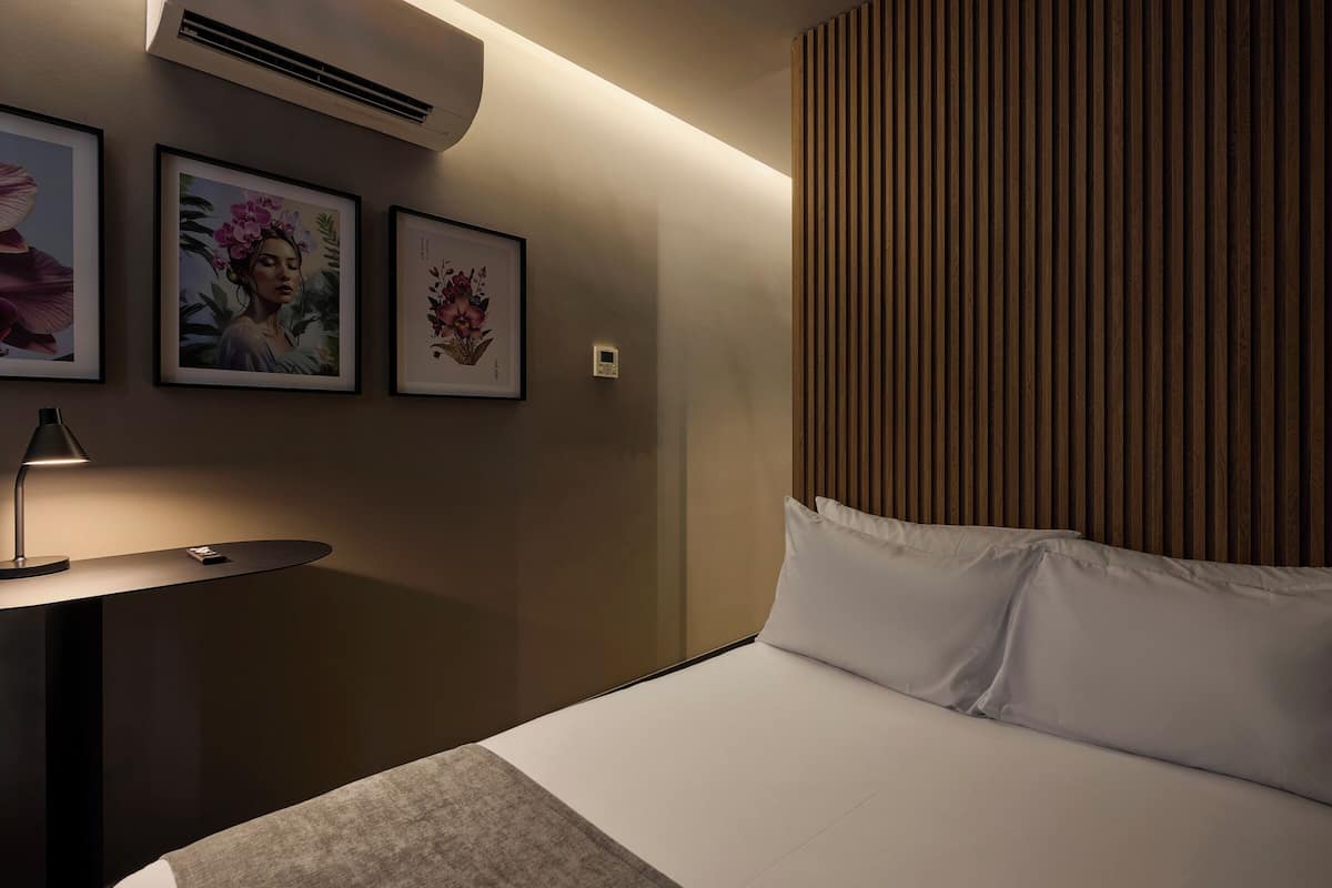 A hotel room with a bed, a bedside table with a lamp, and framed artwork on the wall.