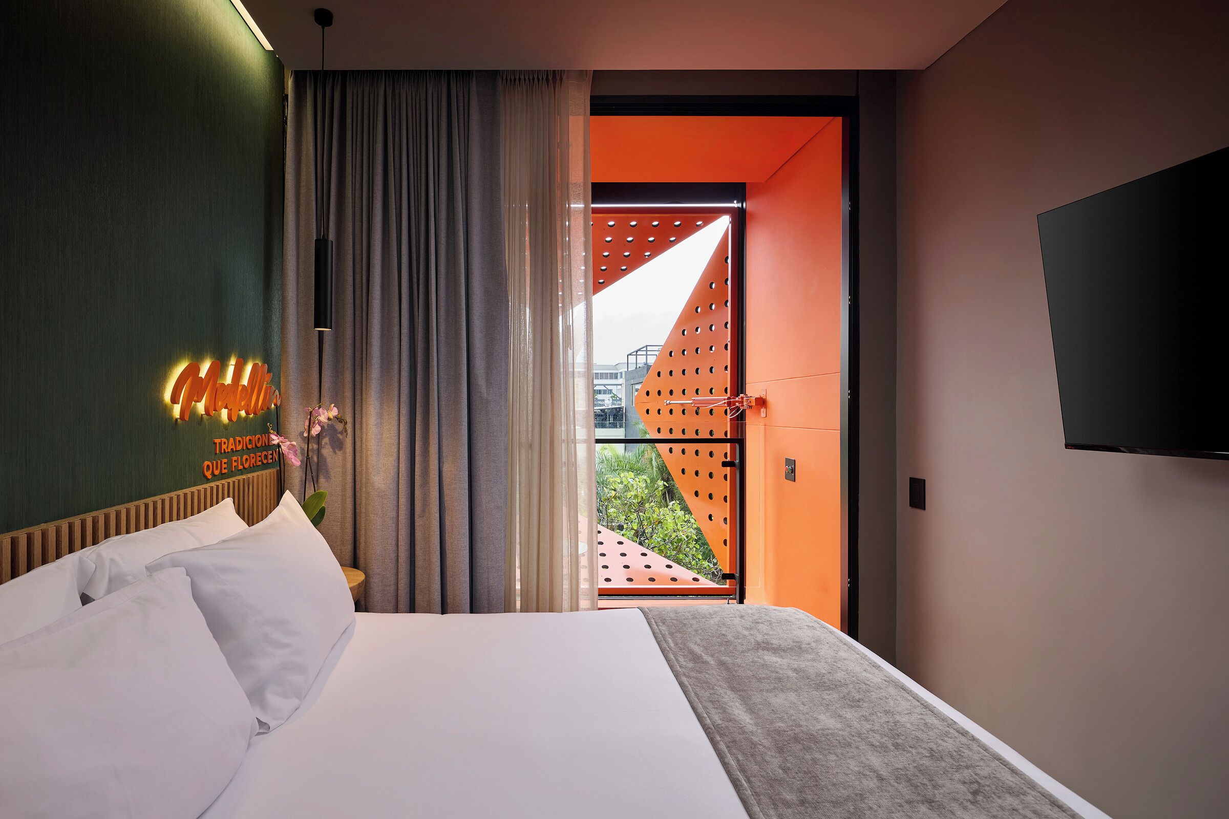 Habitación de hotel con cama, televisor montado en la pared y vista al exterior a través de una puerta.