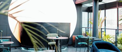 A modern interior with round tables, teal chairs, and a large circular light fixture.