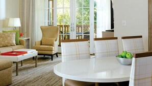 Una sala de estar bien iluminada con un sofá, un sillón y una mesa redonda con un cuenco de manzanas verdes.