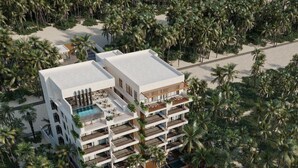 Un hotel de varios pisos con piscina, zona de descanso en la playa y palmeras.