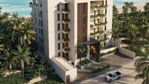 Un hotel moderno con techo plano, varios balcones con plantas y vista a la playa y al océano.
