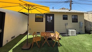 Ein kleines Haus mit einer Terrasse, einem gelben Sonnenschirm und einem Rasen.