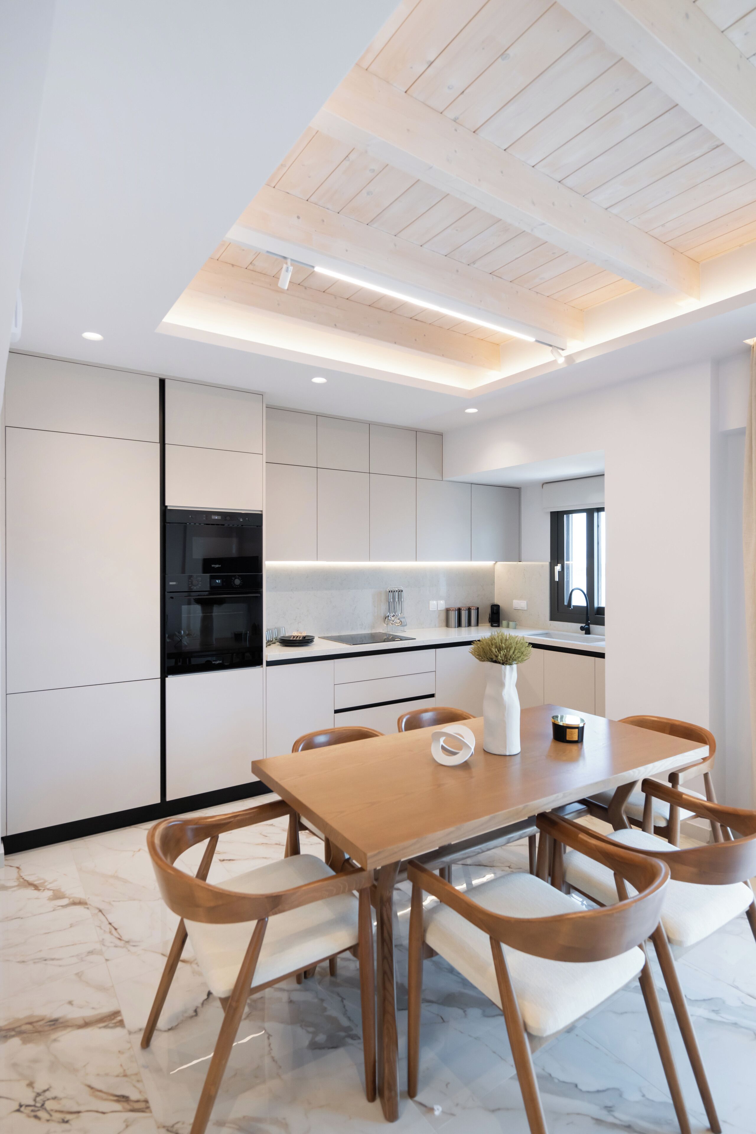 A modern kitchen with white cabinetry, a wooden dining table, and chairs.
