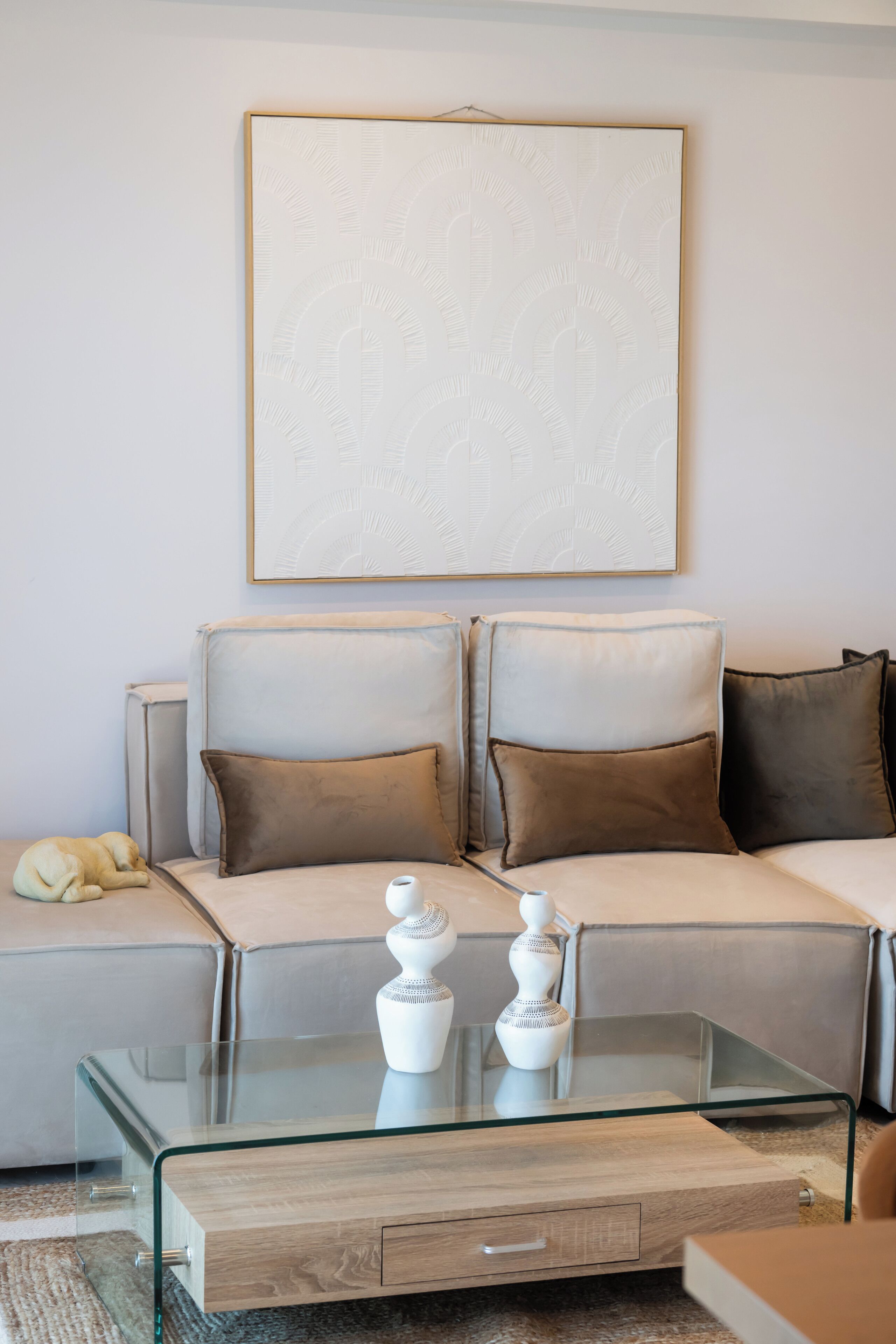 A modern living room with a sofa, cushions, a glass coffee table, and a decorative vase.