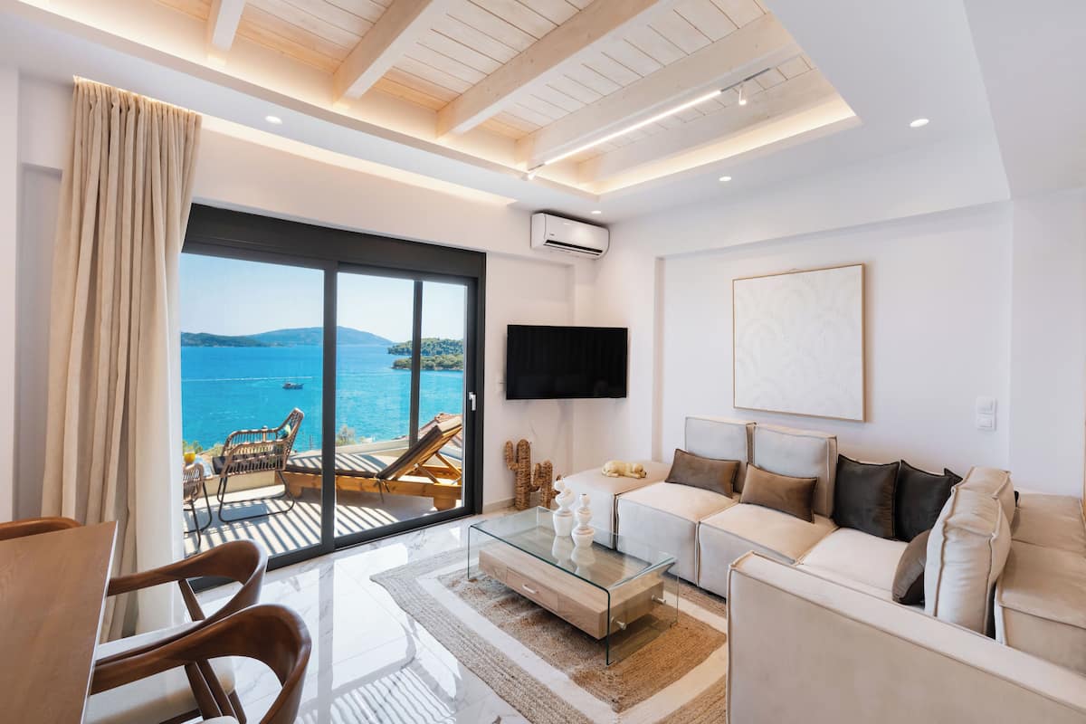 Una sala de estar moderna con un gran ventanal que da a un balcón con vistas panorámicas del mar y las colinas.