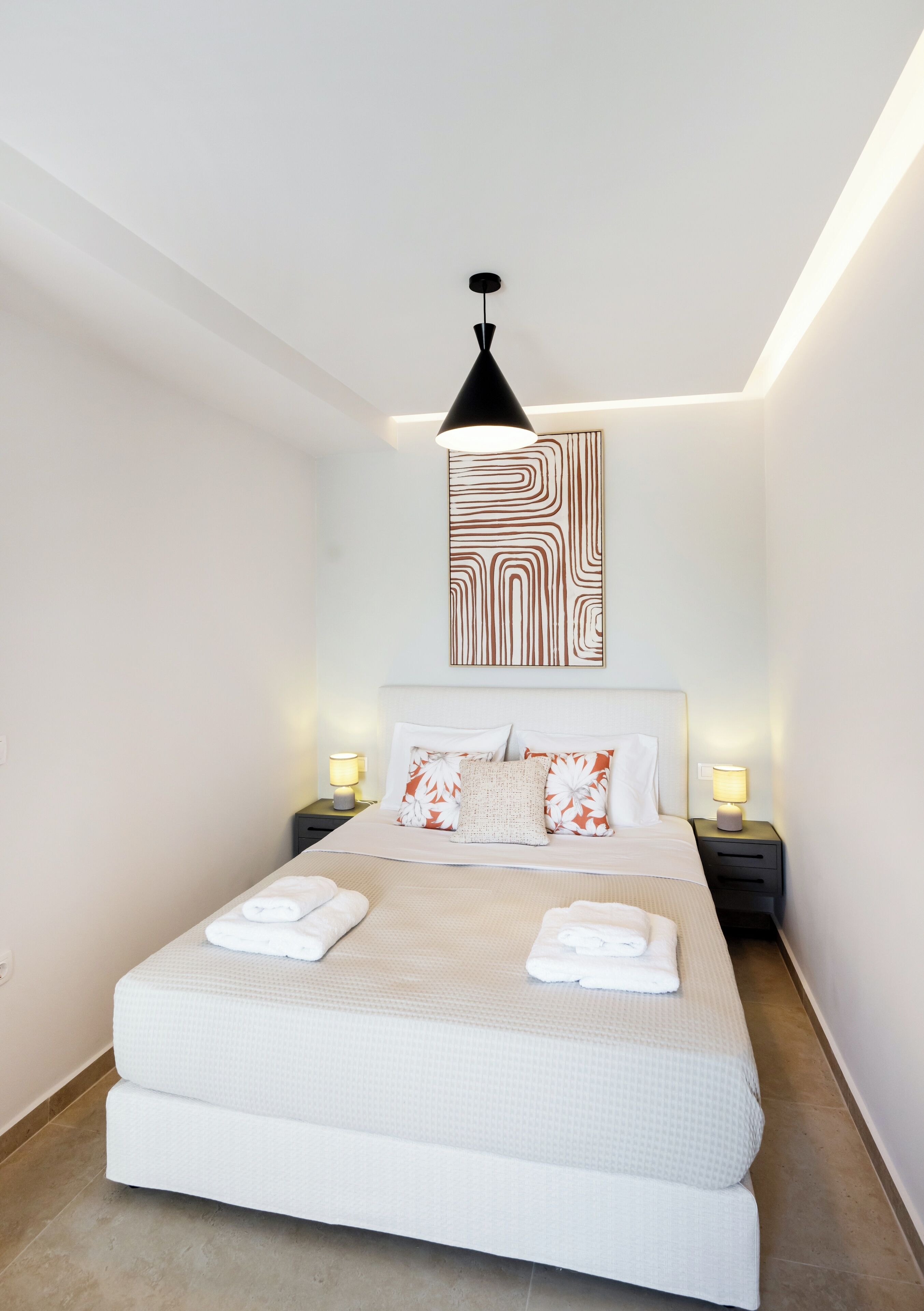 Ein modernes Schlafzimmer mit einem großen Bett, zwei Nachttischen mit Lampen und einem geometrischen Wandbild darüber.