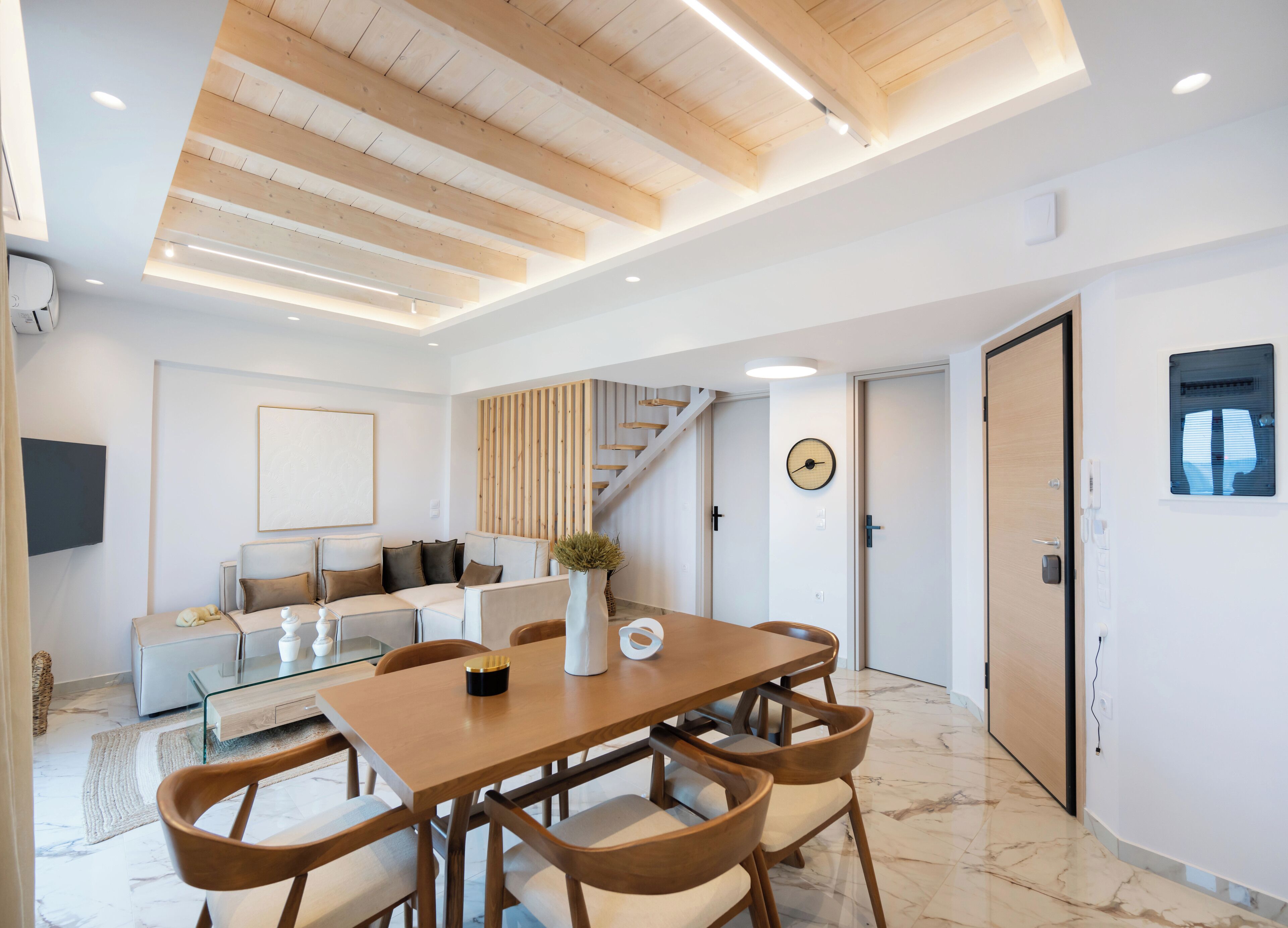 Un salon moderne avec un plafond en bois, un escalier, un coin repas comprenant une table et des chaises en bois, et une décoration minimaliste.