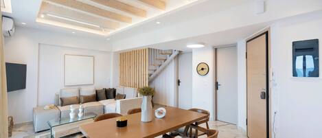 Una sala de estar moderna con techo de madera, una escalera, un comedor con mesa y sillas de madera, y una decoración minimalista.