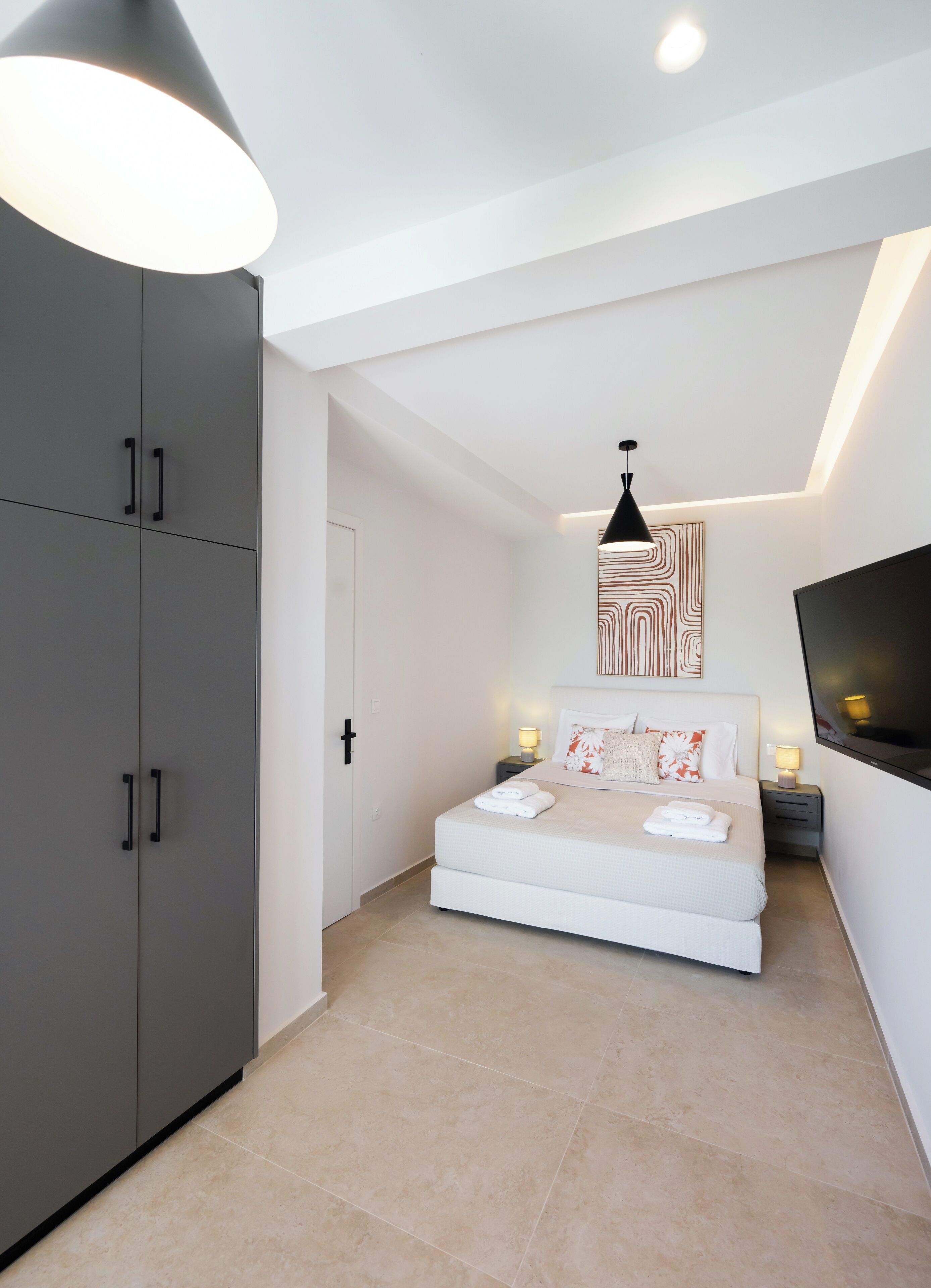A modern bedroom with a bed, a wardrobe, a TV, and a pendant light.