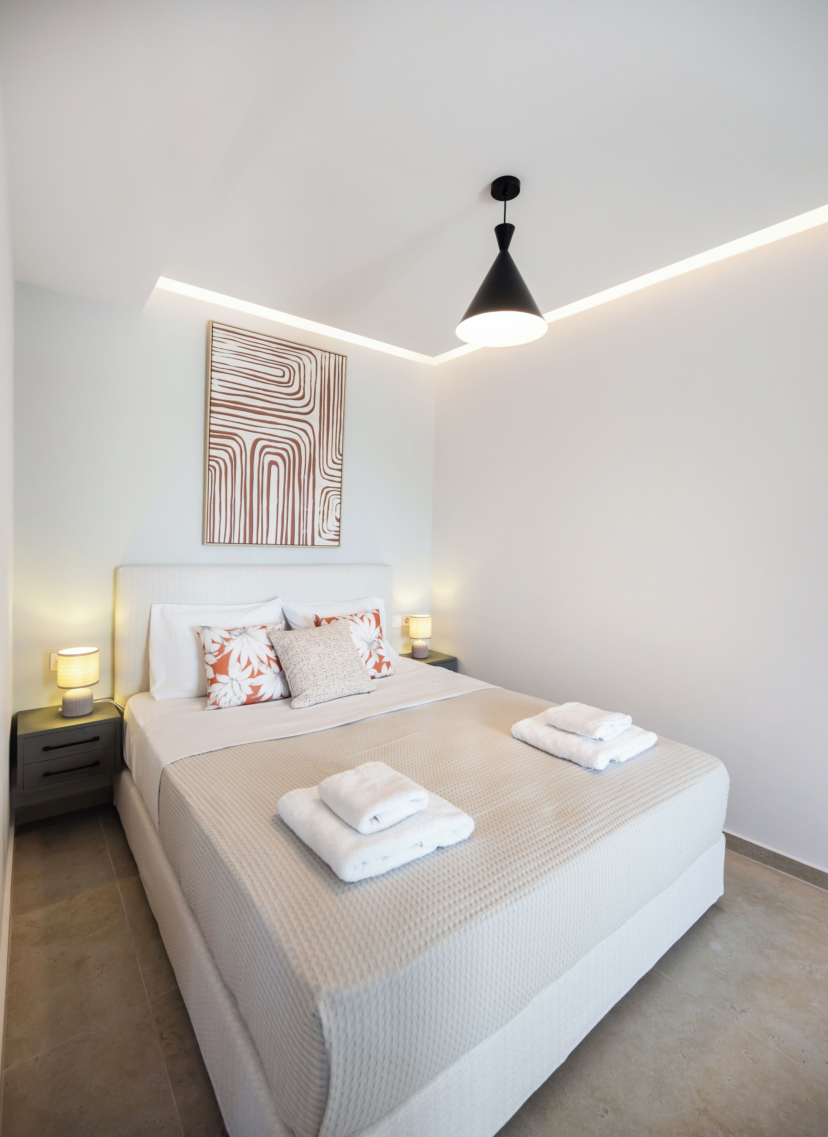 A modern hotel room with a large bed, two bedside tables with lamps, a wall art piece, and a ceiling light fixture.