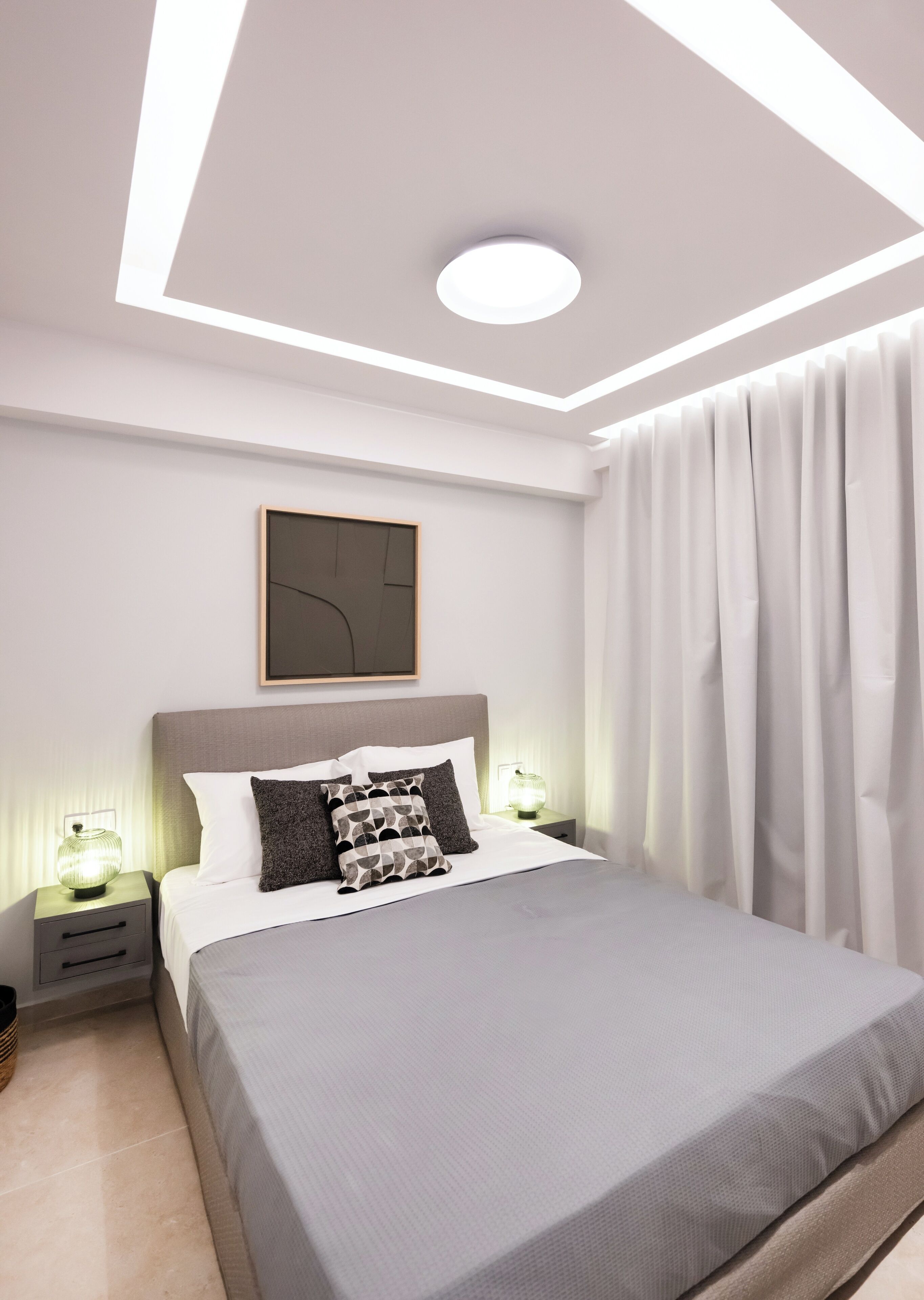 Un dormitorio moderno con una cama grande, una mesita de noche con lámpara, una obra de arte en la pared y un candelabro en el techo.