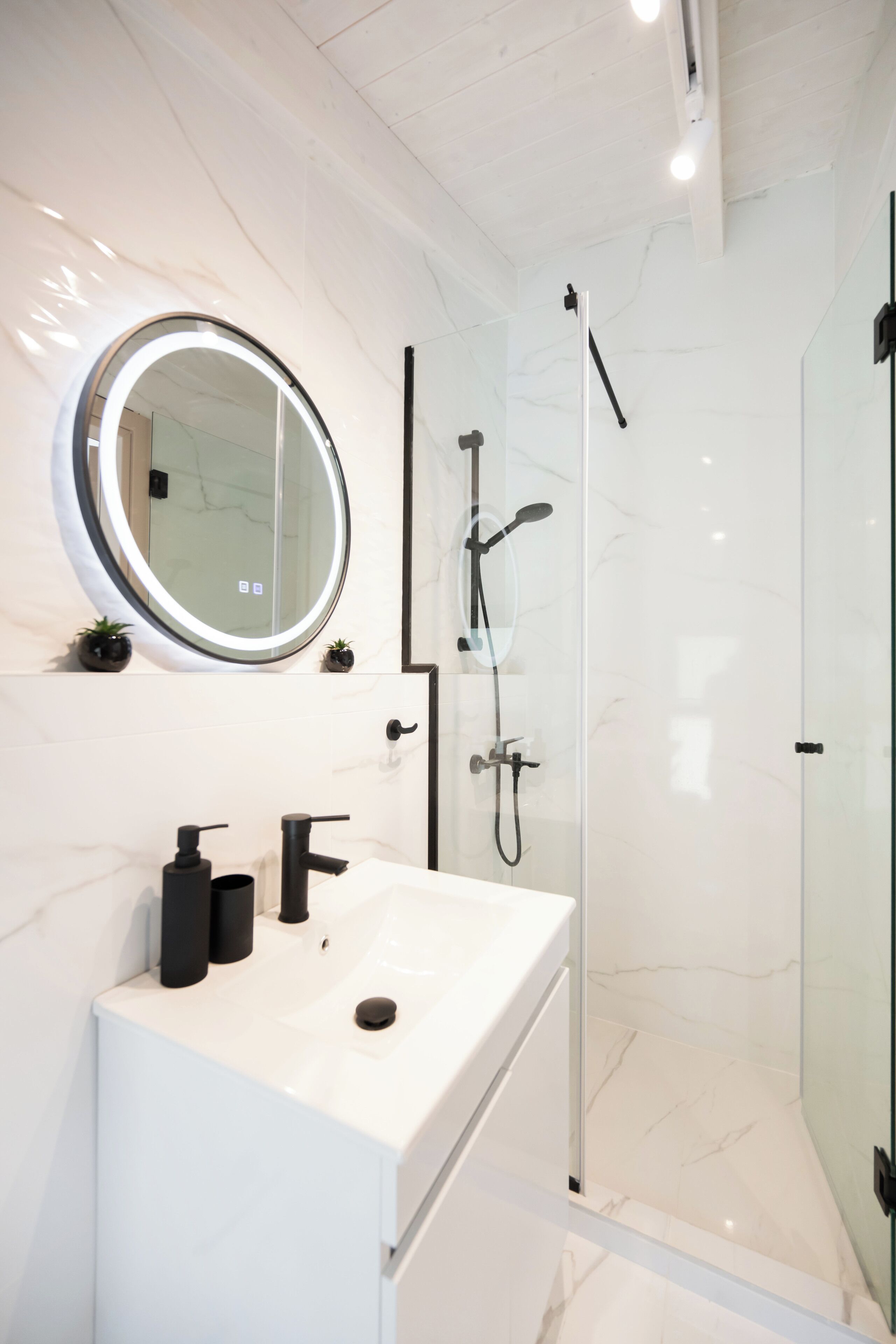 A modern bathroom with a white marble sink, a round mirror, and a glass-enclosed shower.