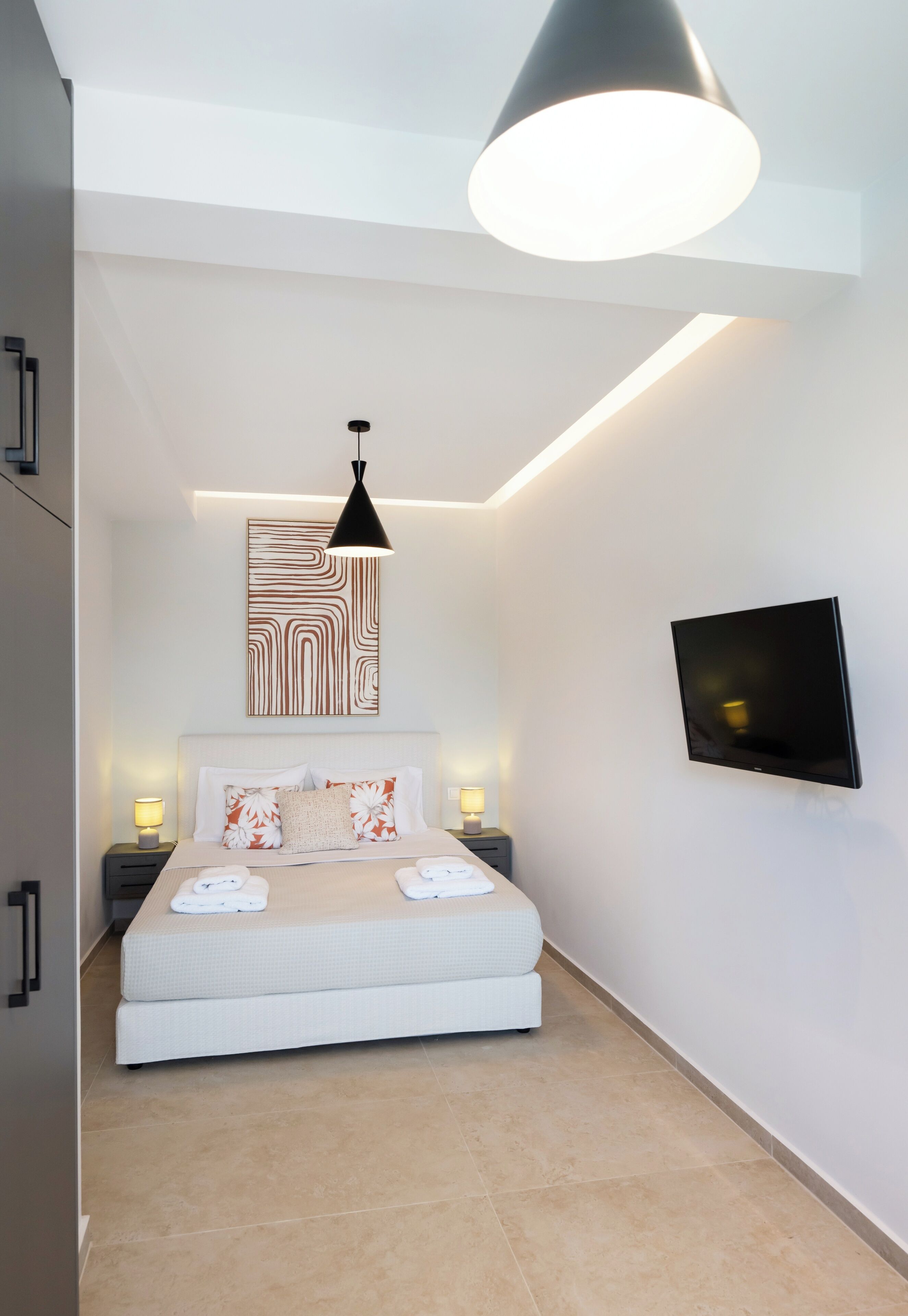 A modern bedroom with a large bed, a flat-screen TV, a pendant light, and a wall-mounted artwork.