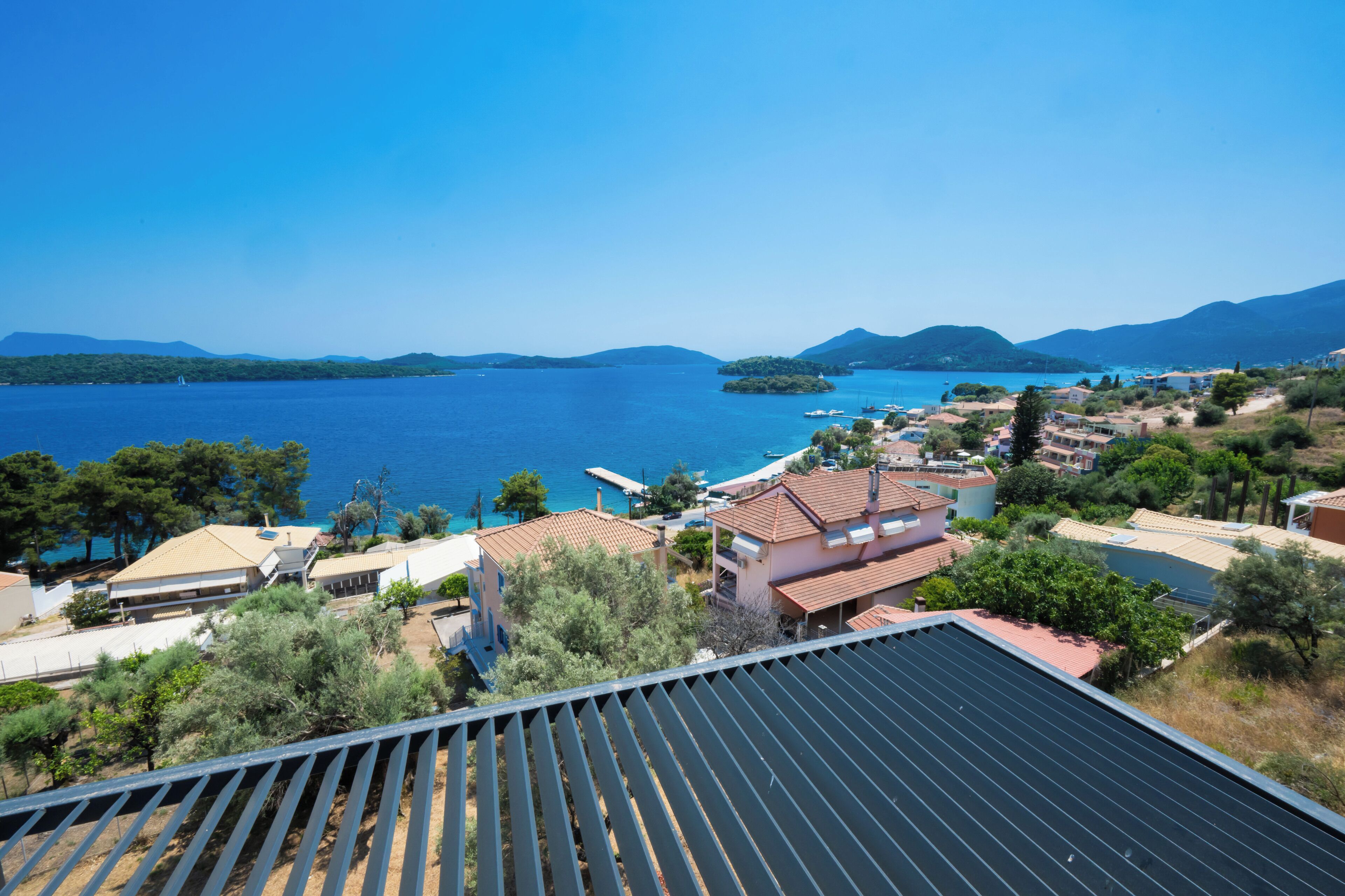 A coastal view with a clear blue sky, a large body of water, and a residential area with houses and trees.