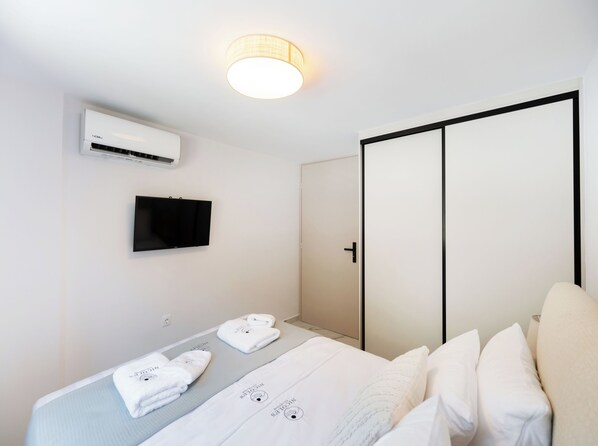 A hotel room with a bed, a TV mounted on the wall, an air conditioning unit, and a wardrobe. - Nicole's Luxury Collection (Lefkada)