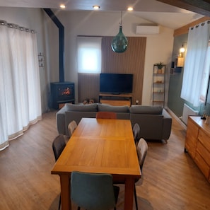A modern living room with a wooden dining table, grey sofas, and a TV.