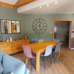 A dining area with a wooden table, chairs, a large wall clock, and a mirror.