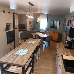 A modern kitchen with wooden countertops, a dining area with a wooden table, and a living area with a sofa and TV.