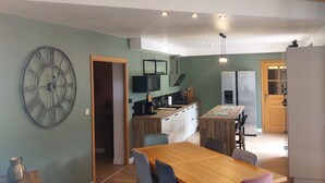 A dining area with a wooden table and chairs, a kitchen in the background, and a large wall clock. - Vacation cottage with heated pool in the heart of the Ibie Valley. (Saint-Maurice-d'Ibie)