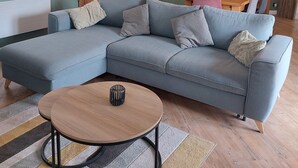 A living room with a sectional sofa, a round coffee table, a wooden dining table, and a large wall clock. - Vacation cottage with heated pool in the heart of the Ibie Valley. (Saint-Maurice-d'Ibie)