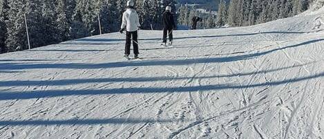 Pista de esquí nevada con esquiadores y una vista despejada de montañas distantes.