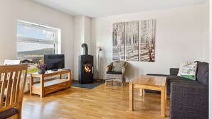 A living room with a wood-burning stove, a TV, a sofa, and a painting of trees. - Stunning view, ski-in/ski-out, 3 bedrooms – Valdres (Aurdal)