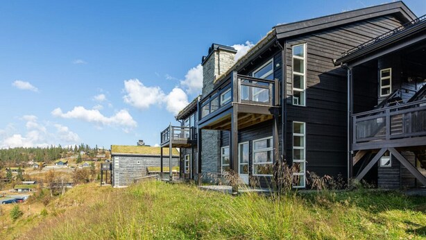 A modern two-story house with a balcony, a stone chimney, and a view of a hilly landscape. - Stunning view, ski-in/ski-out, 3 bedrooms – Valdres (Aurdal)