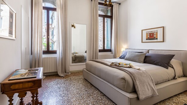 Un dormitorio con cama, mesita de noche, espejo y una araña.