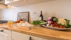Una encimera de cocina con diversos productos frescos, una botella de vino y un cuadro enmarcado.