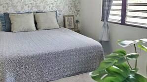 A bedroom with a bed, a window with blinds, a plant, and a wall with a floral pattern. - Cozy studio in charming Aguadilla with AC, WiFi (Aguadilla)