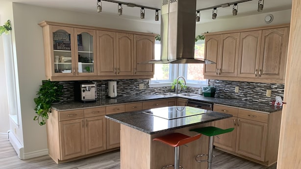 A modern kitchen with wooden cabinets, a central island with stools, and a stainless steel range hood. - The Liberty House (Elegant, Stylish, Spacious) (Charlottetown)